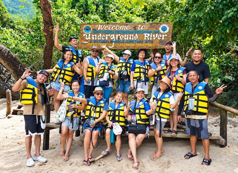 A group of people wearing life vests and standing in front of a sign that reads 'Welcome to Underground River.' 1
