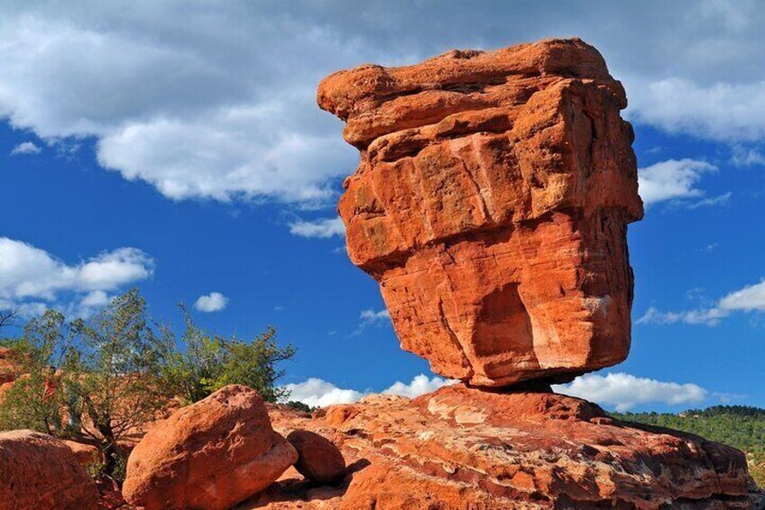 Imponente formazione rocciosa rossa, bilanciata su un'altra roccia, con cielo azzurro e vegetazione rada sullo sfondo. 4
