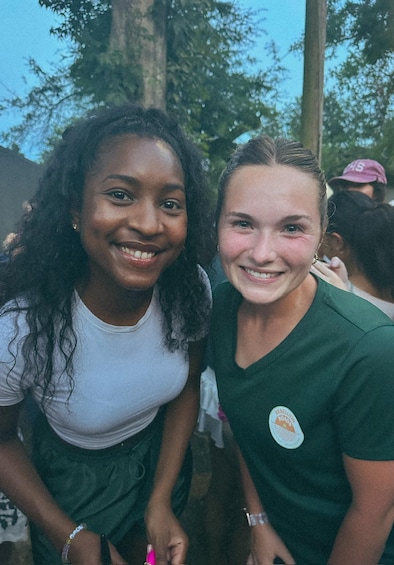 Two people wearing green shirts with a badge, sitting outdoors with trees in the background. 5