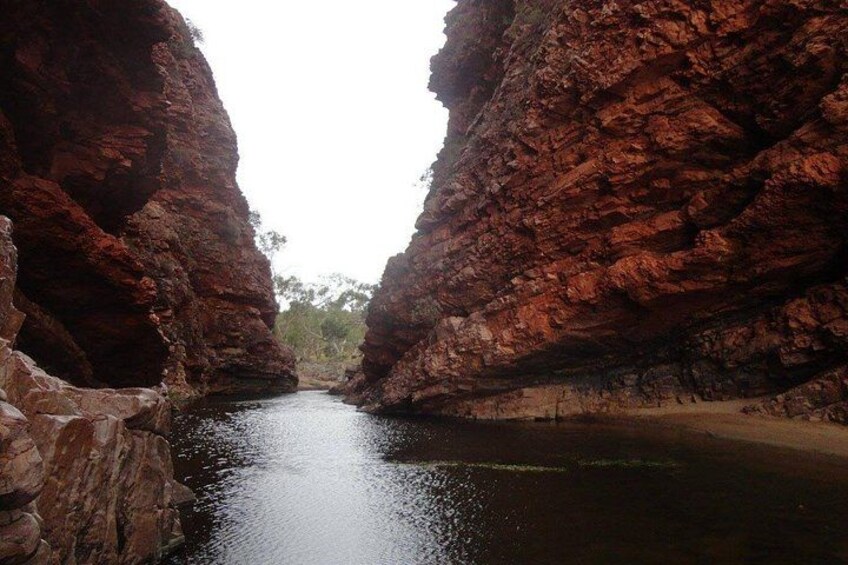 A narrow canyon with steep red rock walls and a calm river. 3