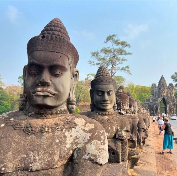 A row of ancient stone statues with intricate carvings, set against a backdrop of a clear sky and distant temple structures. 4