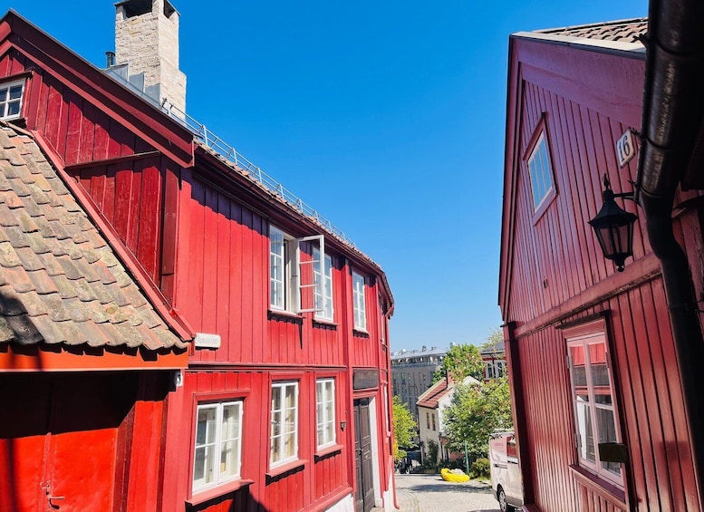A narrow street with red wooden buildings, a clear blue sky, and a visible chimney on the left building. 5