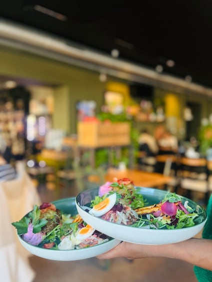 Two plates of salad with various greens and a boiled egg, held by a person. 1