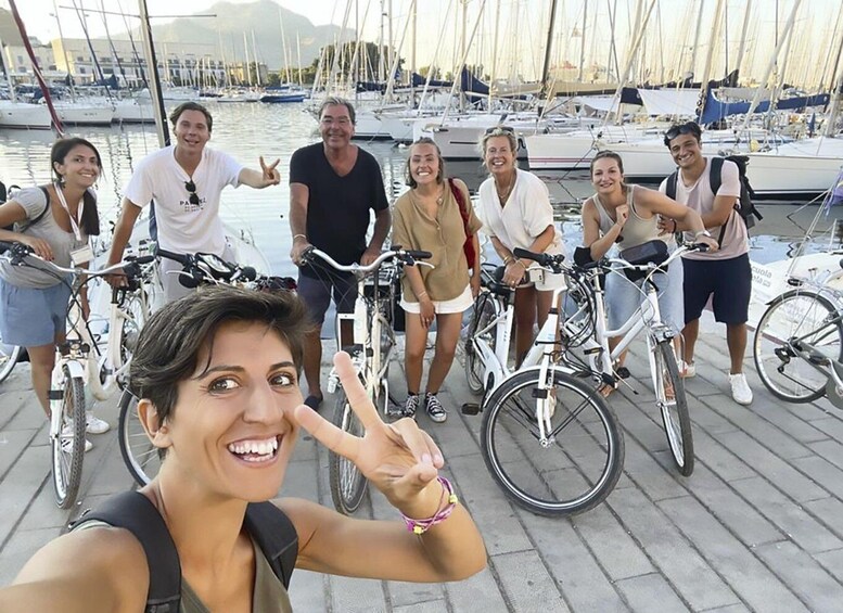 A group of people posing with bicycles in a marina with boats in the background. 2