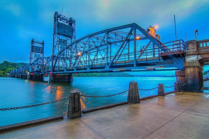 A large steel bridge over a body of water with a chain barrier in the foreground. 1