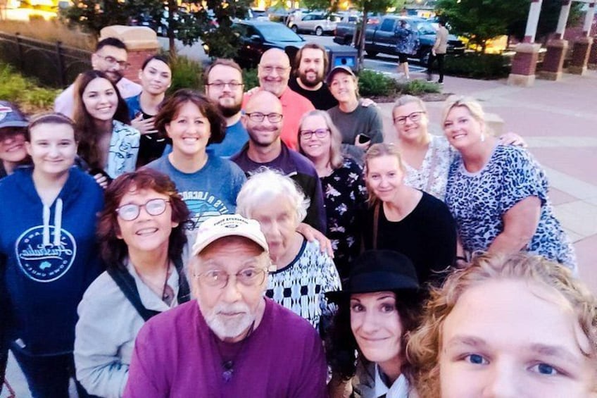 Un grupo de personas reunidas al aire libre, algunas con ropa informal, con una calle y coches aparcados al fondo. 5