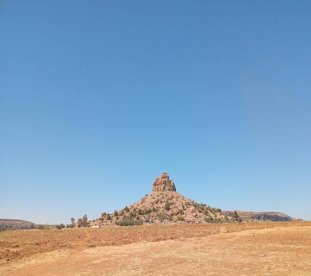 A clear blue sky, a dry, barren landscape with a prominent rocky hill in the center, and sparse vegetation. 4