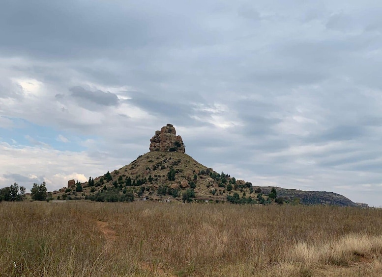 A rocky hill with a prominent peak, surrounded by sparse vegetation and a cloudy sky. 2