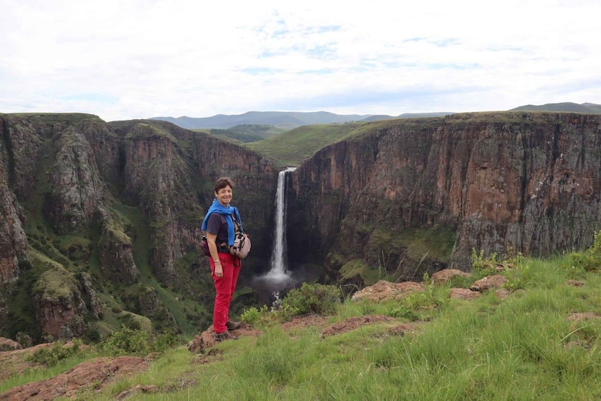 A person standing on a grassy hill overlooking a deep canyon with a waterfall. 5