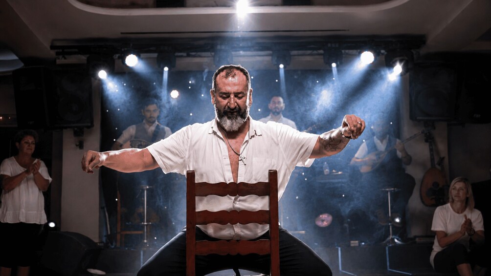 A person seated on a chair with arms outstretched, surrounded by a group of people. 2