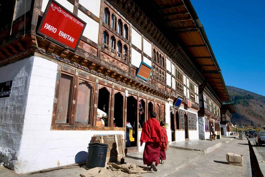 Ein traditionelles Gebäude mit einem Schild, auf dem 'PARO BHUTAN' steht, und ein Mönch, der davor entlanggeht. 1