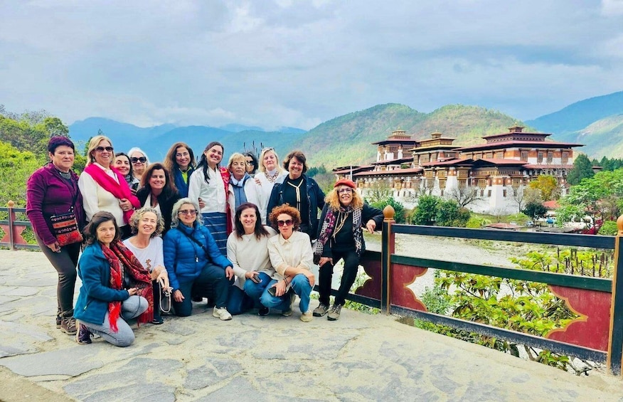 A group of people posing in front of a traditional building with a mountainous backdrop. 1