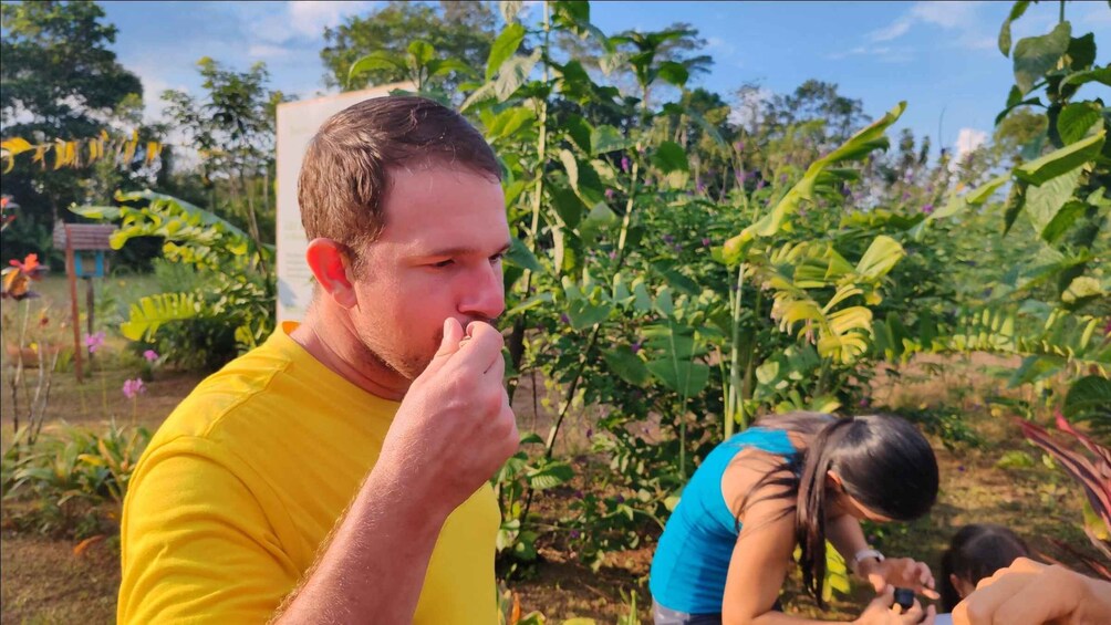 A person in a yellow shirt eating in a garden with various plants and a child in the background. 3