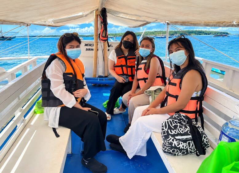 Vier Personen in einem Boot mit Schwimmwesten, ruhige See und eine Insel im Hintergrund. 3