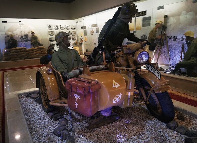 A motorcycle with a sidecar, a helmeted rider, and a soldier in the background. 5