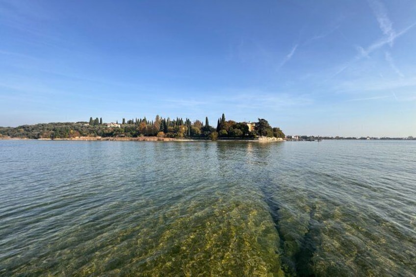 Un lago tranquilo con aguas transparentes, una orilla lejana con árboles y edificios, y un cielo azul despejado. 3