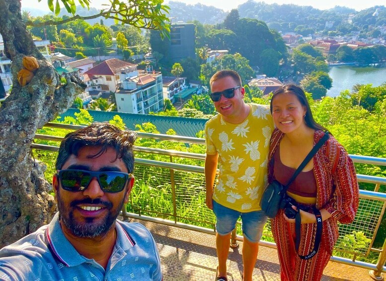 Drei Personen stehen auf einem Balkon mit Blick auf einen Fluss und Gebäude. 3