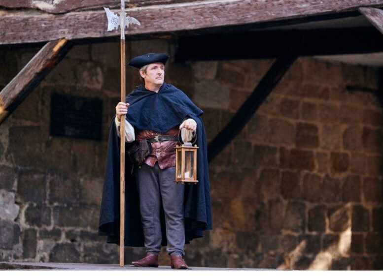 A person in historical costume holding a lantern and a staff. 1