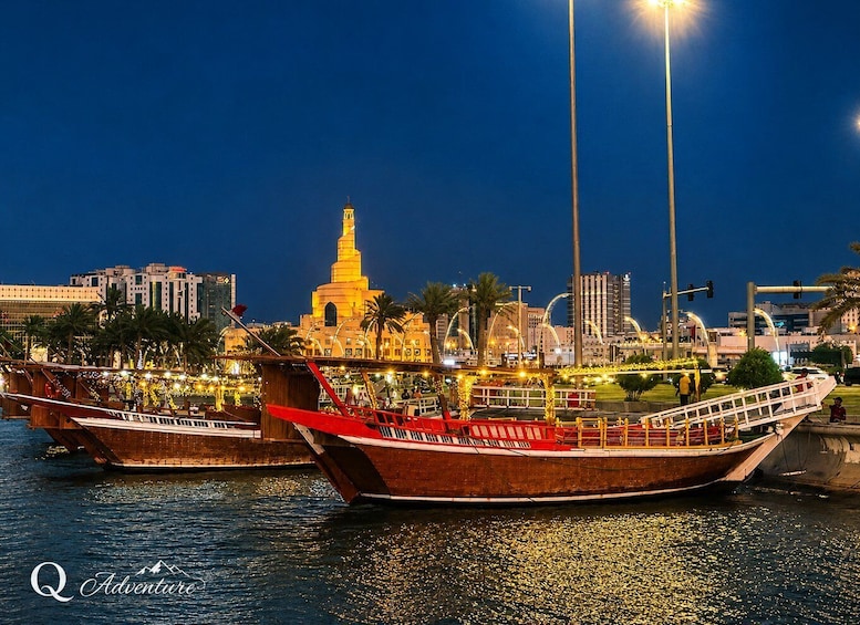 Traditional wooden boats docked at a marina with a city skyline and a prominent tower in the background. 1