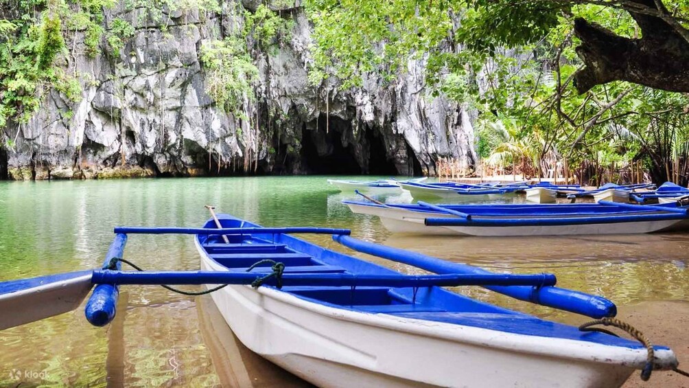 A row of traditional boats docked at a calm river with a rocky cliff in the background. 2