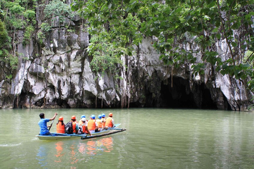 A group of people in a boat on a calm river, surrounded by rocky cliffs and lush greenery. 3