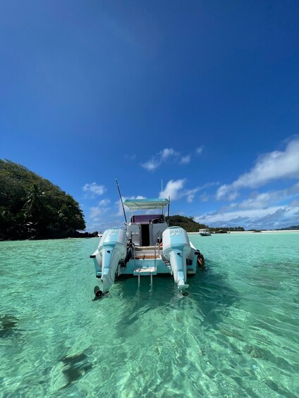 A boat anchored in clear turquoise waters with a lush island in the background. 5