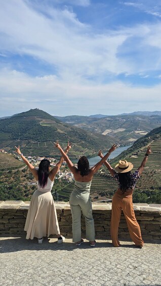 Three people standing on a stone wall overlooking a valley with terraced fields and a river. 3