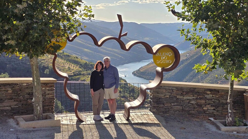 A couple standing in front of a sign with a scenic view of a river and mountains in the background. 5