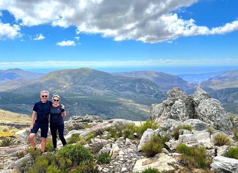 Two people standing on a rocky outcrop with a mountainous landscape in the background. 3