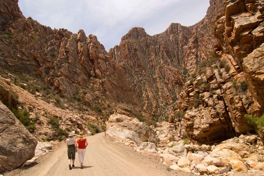 A narrow canyon road with rocky terrain and a couple walking. 2