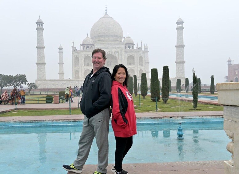 A couple standing in front of the Taj Mahal with a pool and trees in the foreground. 3