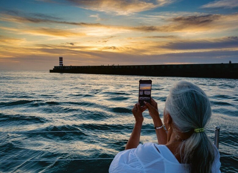 A person taking a photo of a sunset over the ocean with a pier in the background. 5
