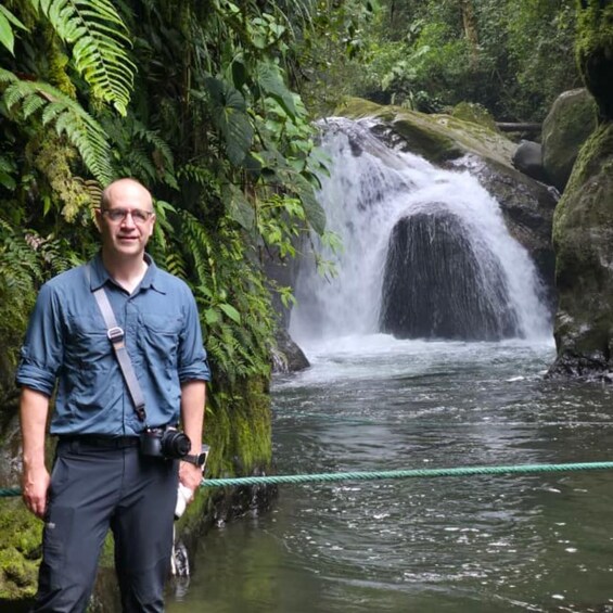 A man standing by a waterfall surrounded by lush greenery. 4