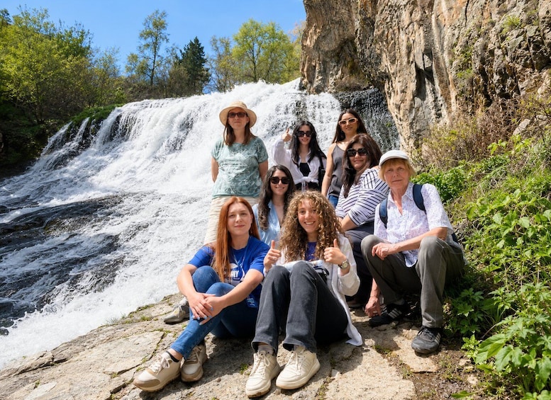 A group of people sitting by a waterfall surrounded by greenery. 1