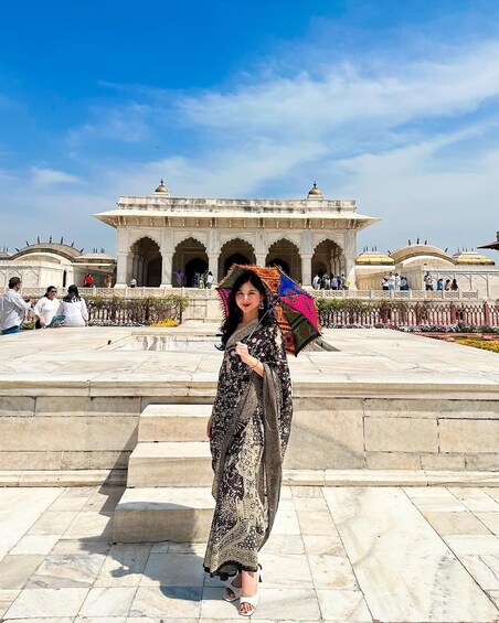 Une femme, vêtue d’un costume traditionnel, se tient devant un bâtiment historique orné d’arches et de coupoles. 5