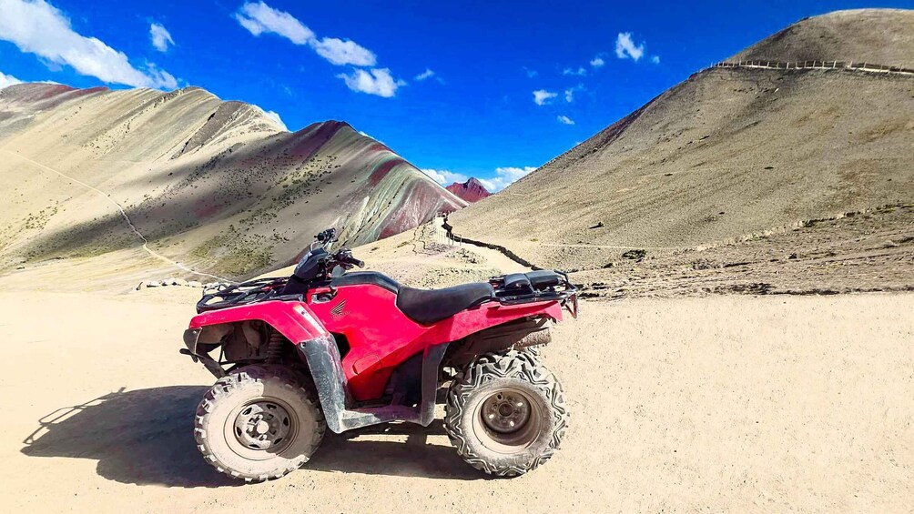 A red ATV parked on a dirt road with mountains in the background. 2