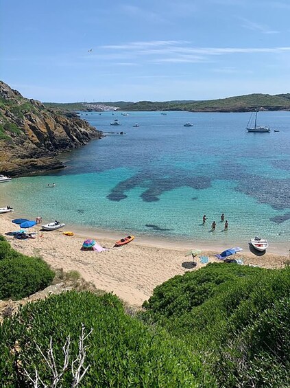 A coastal beach with clear turquoise water, boats, and people swimming. 5