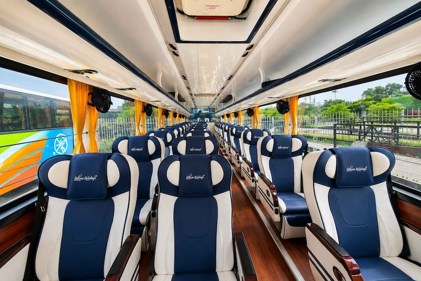 Een treininterieur met rijen blauwe en witte stoelen, een nooduitgangsbordje en een uitzicht op groen. 3