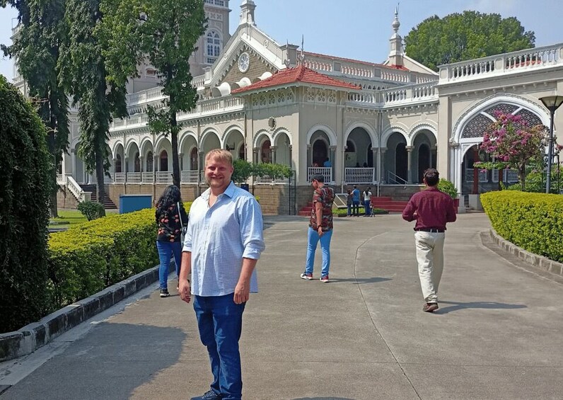 A man standing in front of a large, ornate building with arched walkways and a red-tiled roof. 4