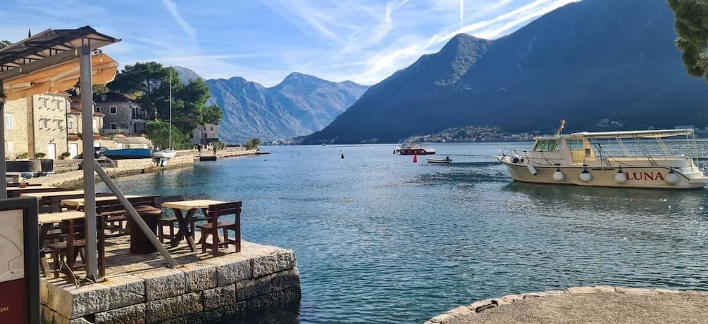 A lakeside town with a dock, a boat named 'LUNA,' and mountains in the background. 2