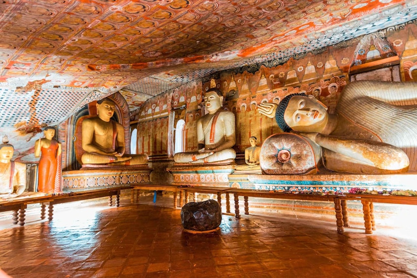 A temple interior with large Buddha statues, intricate ceiling artwork, and a stone in the center. 2
