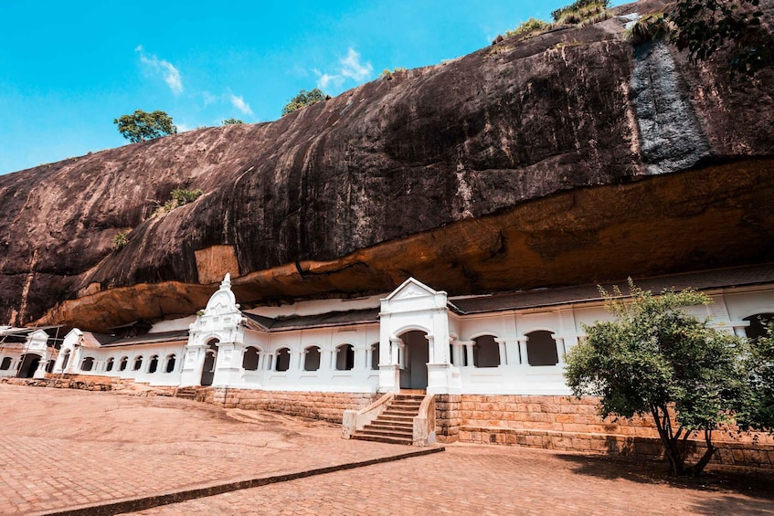 A white temple with a staircase leading up to it, set against a large rock formation. 5