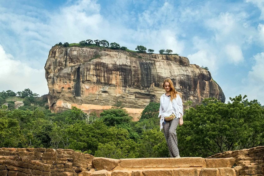 A person standing in front of a large rock formation with trees in the background. 3