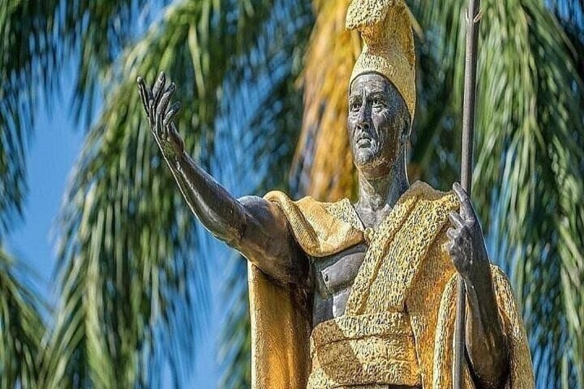 Una statua raffigura una figura in abiti tradizionali con una lancia, sullo sfondo di palme. 3