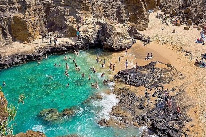 Une plage rocheuse aux eaux turquoise et limpides, où l’on peut voir des gens nager et prendre des bains de soleil. 2