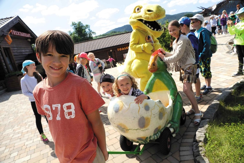 A child in a red shirt with the number 978, a dinosaur mascot, and a dinosaur-themed ride. 2