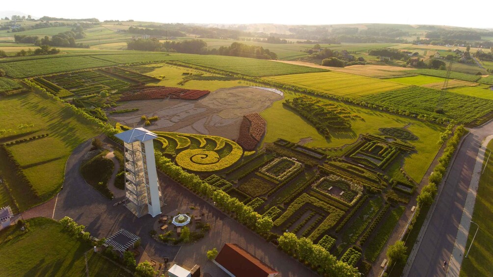 An aerial view of a landscaped estate with formal gardens, a tall building, and surrounding fields. 4