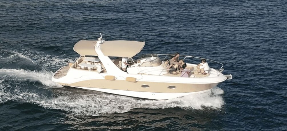 A white motorboat with a canopy, passengers, and wake on the water. 2