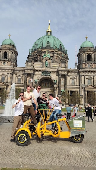 A group of people on a yellow sightseeing bike in front of a historic building with green domes. 2
