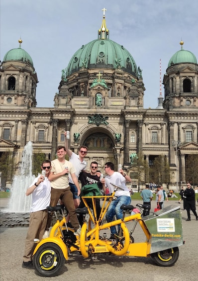 A group of people on a yellow bicycle tour bike in front of a historic building with green domes. 3